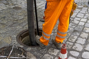 Kanalschacht mit Schlauch zum Absaugen und Arbeiterbeinen