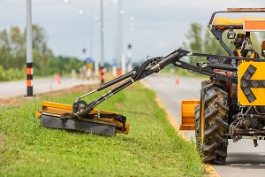 mowing unit at the extension arm of a tractor, mowing grass on the median of a road