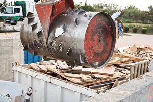waste compactor on an extension arm above a container with waste wood