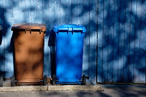 brown and blue garbage cans in front of a wooden wall